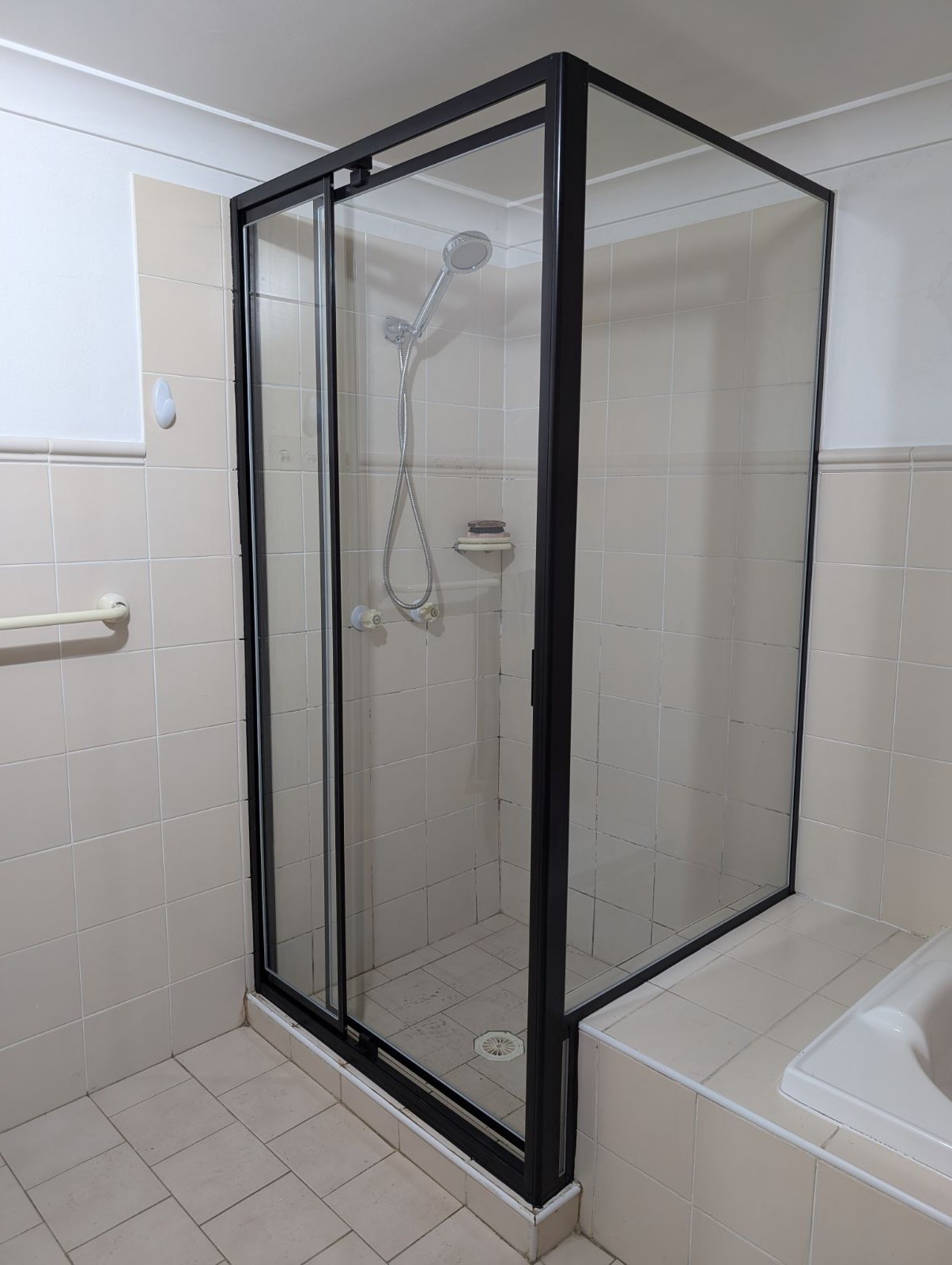 Custom dog-leg shower screen over a bath with black hardware, Sydney