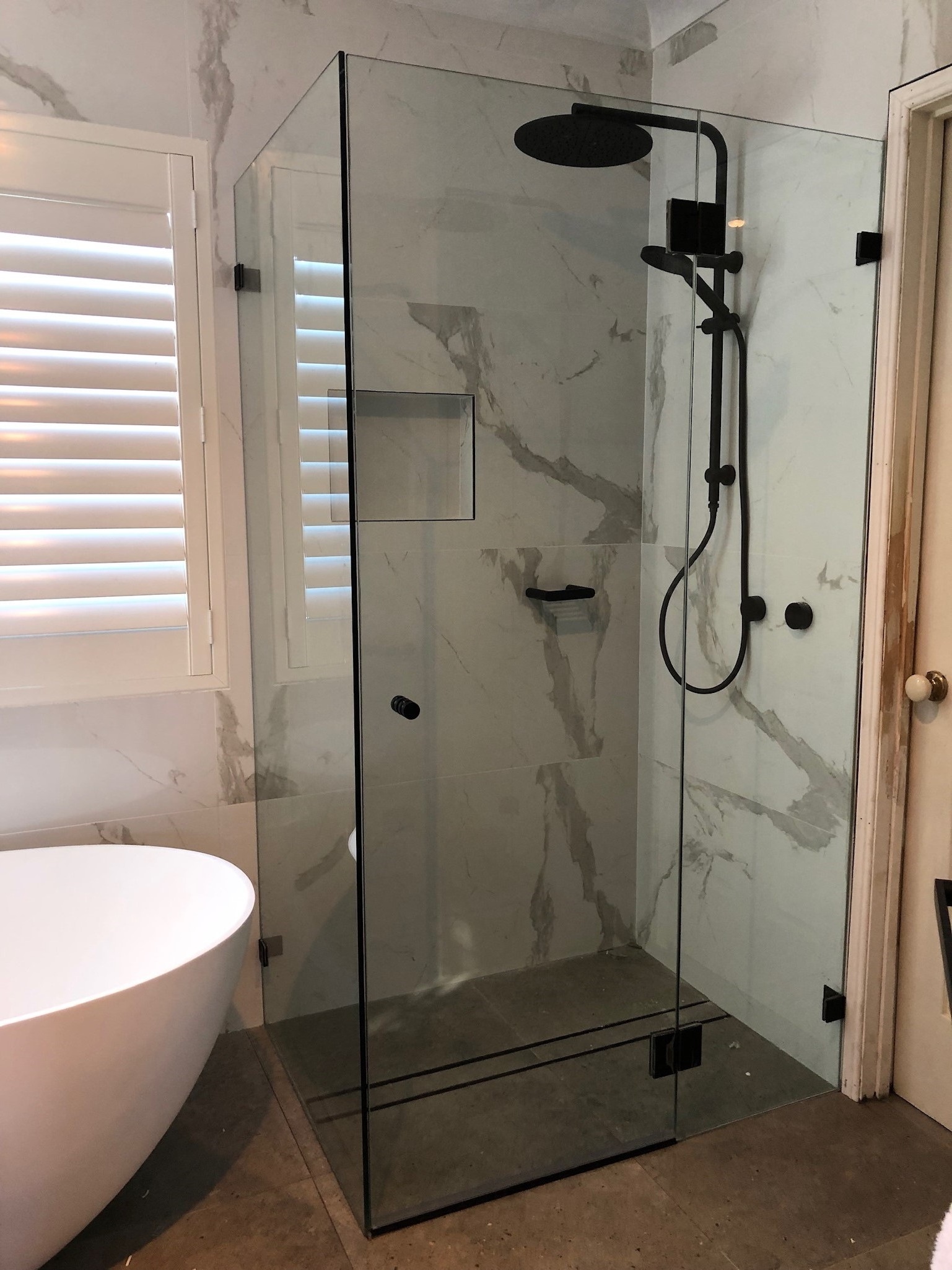 Premium frameless shower screen with marble tiles and matte black fittings
